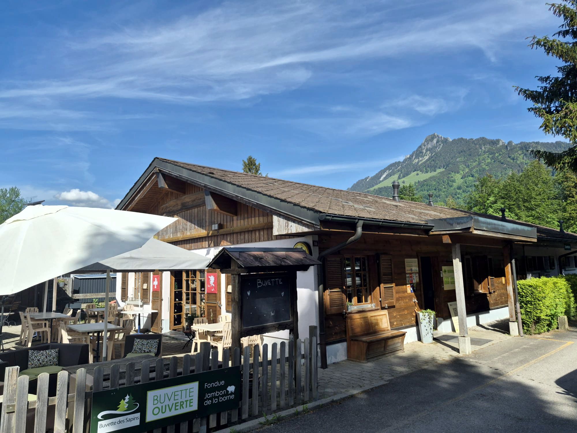 Le chalet du restaurant Buvette des Sapins à Epagny et sa terrasse sous le ciel bleu, montagne de Gruyère en arrière-plan